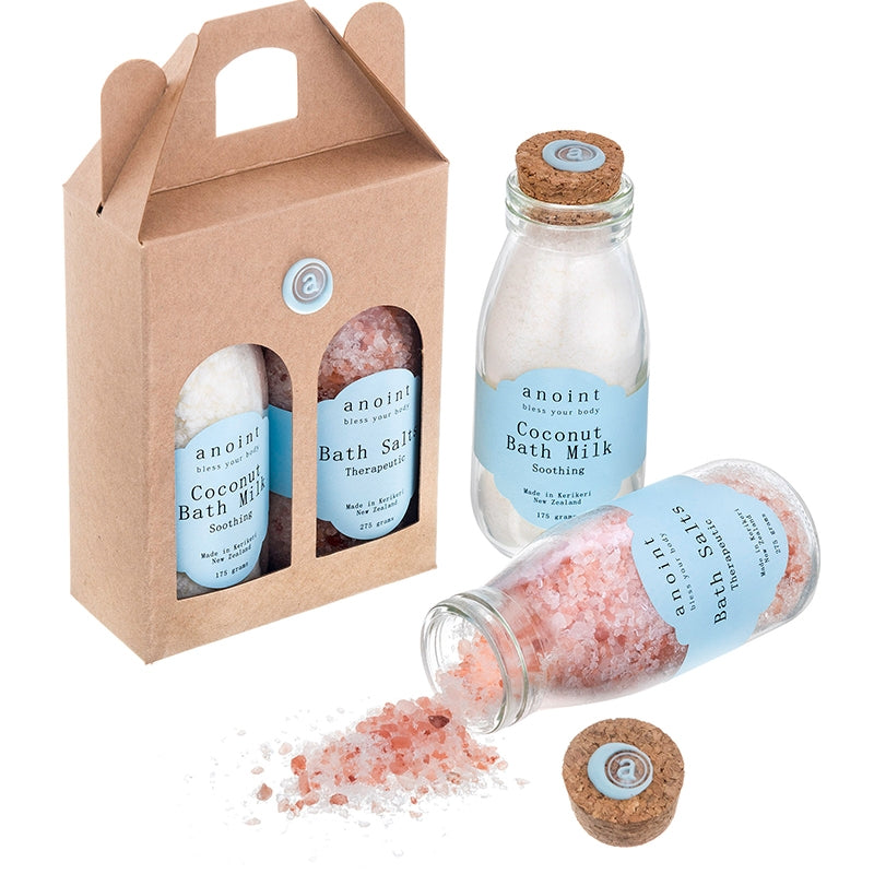 Two sets of bath milks and bath salts. One in a gift box and one open and scattered to show the contents.